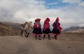 Three native women walk and talk leading a horse as they walk on a dirt road wearing