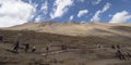 Tourists walk down dirt path next to mountain range under blue sky