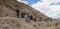 Trekkers walk down dirt path next to mountain under blue sky