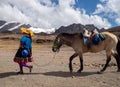 Young native woman leading horse with snow covered mountains on the background