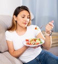 Peruvian housewoman eating vegetable salad on sofa at home