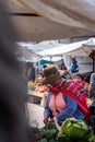 Peruvian woman carrying her child on the back in traditional way buying groceries on local market from Pisac, Peru