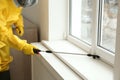 Pest control worker in protective suit spraying pesticide near window, closeup Royalty Free Stock Photo