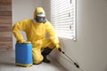 Pest control worker in protective suit spraying pesticide near window Royalty Free Stock Photo