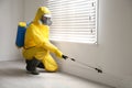 Pest control worker in protective suit spraying pesticide near window Royalty Free Stock Photo