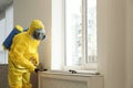 Pest control worker in protective suit spraying pesticide near window Royalty Free Stock Photo