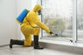 Pest control worker in protective suit spraying pesticide near window Royalty Free Stock Photo