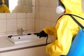 Pest control worker spraying pesticide near sink in restroom