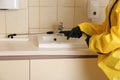 Pest control worker spraying pesticide near sink in restroom