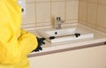 Pest control worker spraying pesticide near sink in restroom