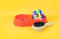 Brush and rubber toy in plastic bowl for pet on yellow background Royalty Free Stock Photo