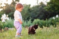 Pet care. Cute toddler girl standing next to a black cat. In the background, green grass and garden plants. In the Royalty Free Stock Photo