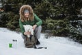 Pet care in winter cold season. Happy woman and Maltese dog in backpack walking, having fun and drinking hot tea Royalty Free Stock Photo