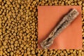 Pet food and chew treats. A stick of dried beef tripe lies on a piece of paper. Brown pellets of dry dog food. A square sheet of