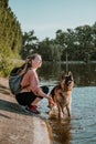 Pet Love. Young sports happy woman plays with German Shepherd dog near lake. Authentic moments of joy girl playing with her dogs. Royalty Free Stock Photo