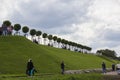 Row of manicured Tilia trees in line on and people walking on green grass lawn hill of Garden of Venus with blue sky