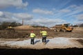 Two workers in high vis jackets and hard hats on a construction site with dumper digger truck Royalty Free Stock Photo