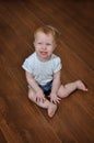 Petite crying baby girl sitting indoor on the wooden floor