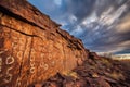 petroglyphs on a cliff face with dramatic sky background