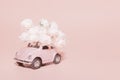 Petrozavodsk, Russia - April 04, 2019: Pink retro toy car with bouquet of white Roses on pink background. Concept Valentine`s day