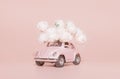 Petrozavodsk, Russia - April 04, 2019: Pink retro toy car with bouquet of white Roses on pink background. Concept Valentine`s day