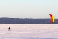 A kiter on skis under a colored dome rides on the big Onega Lake on a hard snow crust.