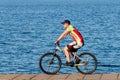 Handsome athletic man on a bike rides along the edge of the embankment against the backdrop of water