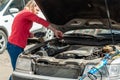 A young woman at the open bonnet of a car is trying to fix the malfunction Royalty Free Stock Photo