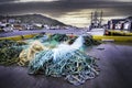 Fish nets piled on a dock with fishing trawlers in a small East Coast town.