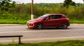 Peugeot 308 five door hatchback is driving at high speed on country road. Overspeed out of city concept. Red car in motion