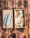 Pharmaceutical drugs pills and syringe vials in box on wooden background, first aid kit