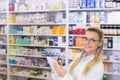 Female pharmacist wearing lab coat holding notepad and checking shelves in pharmacy, copy space Royalty Free Stock Photo