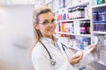 Female pharmacist standing in pharmacy aisle holding prescription slip near medicine shelves Royalty Free Stock Photo
