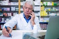 Pharmacist talking on mobile phone while writing prescriptions Royalty Free Stock Photo