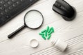 Pharmacological capsules and magnifier with keyboard and computer mouse on a white wooden table