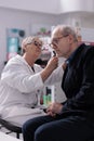 Pharmacy employee checking old man ear with otoscope