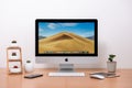 IMac computer, keyboard, magic mouse, plant vase, cactus pots and coffee cup on wooden table