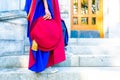 PhD doctoral graduate in regalia gown, holding Tudor bonnet cap, sitting on university steps, with sneaker canvas shoes showing Royalty Free Stock Photo