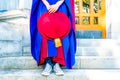 PhD doctoral graduate in regalia gown, holding tudor bonnet cap, sitting on university steps, with sneaker canvas shoes showing