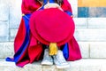 PhD doctoral graduate in regalia gown, holding tudor bonnet cap, sitting on university steps, with sneaker canvas shoes showing