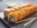 Philadelphia and California rolls on a textured dark plate. Next to it are wasabi, ginger and bamboo chopsticks. Side view, close Royalty Free Stock Photo