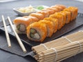 Philadelphia and California rolls on a textured dark plate. Next to it are wasabi, ginger and bamboo chopsticks. Side view, close Royalty Free Stock Photo