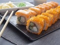 Philadelphia and California rolls on a textured dark plate. Next to it are wasabi, ginger and bamboo chopsticks. Side view, close Royalty Free Stock Photo