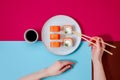 Philadelphia rolls with salmon fish, cucumber and cheese on plate and woman hand with chopsticks on colorful background Royalty Free Stock Photo