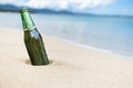 A bottle of Carlsberg Beer partially buried in the sand by a tropical beach