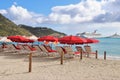 Philipsburg, St. Martin - 1/23/18: Beach umbrellas and lounge chairs along the beach and the Carnival Conquest cruise ship docked Royalty Free Stock Photo