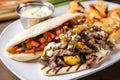 philly cheesesteak with a side of grilled mixed vegetables on a white plate