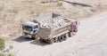 Truck passes by a halted truck on the road leading to the site. The halted truck burdened with stones and a flat rear tire.