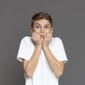 Scared teenager biting fingernails, grey studio background