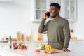 Phone Call. Handsome Young Black Guy Talking On Cellphone In Kitchen Interior Royalty Free Stock Photo